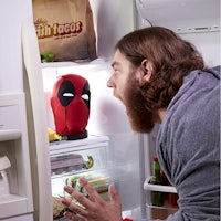 a man is staring at a deadpool head in an open refrigerator